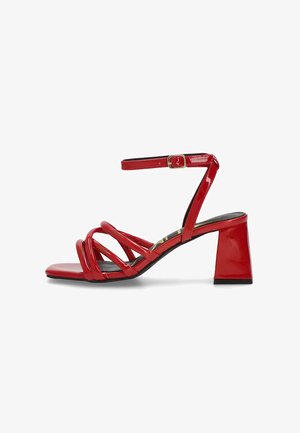 Las sandalias de charol rojo con tacón cuadrado presentan múltiples tiras entrecruzadas y una correa ajustable en el tobillo con una hebilla dorada.