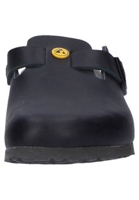 Black rubber clogs feature a smooth surface, two adjustable straps, and a round toe. A yellow logo button is centered on the strap.