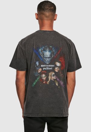 Mand iført en falmet sort T-shirt med farverige Batman & Robin-figurer og logo trykt på bagsiden mod en ensfarvet baggrund.
