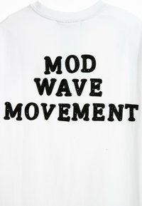 Camiseta de algodón blanca con grandes letras negras que dicen "MOVIMIENTO MOD WAVE", con un diseño texturizado y en relieve en la tipografía.