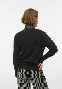 Mörkgrå stickad tröja med långa ärmar, rund halsringning och ribbad fåll, kombinerad med svartvita byxor med mönster.