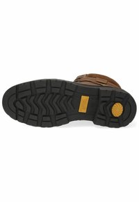 Semelle de bottes en cuir brun avec des crampons profonds, en matériau en caoutchouc noir, détail de logo jaune et motifs texturés pour l'adhérence et la traction.