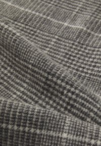 Tissu gris doux avec un motif écossais et pied-de-poule texturé, présenté en gros plan avec des plis et des fibres visibles.