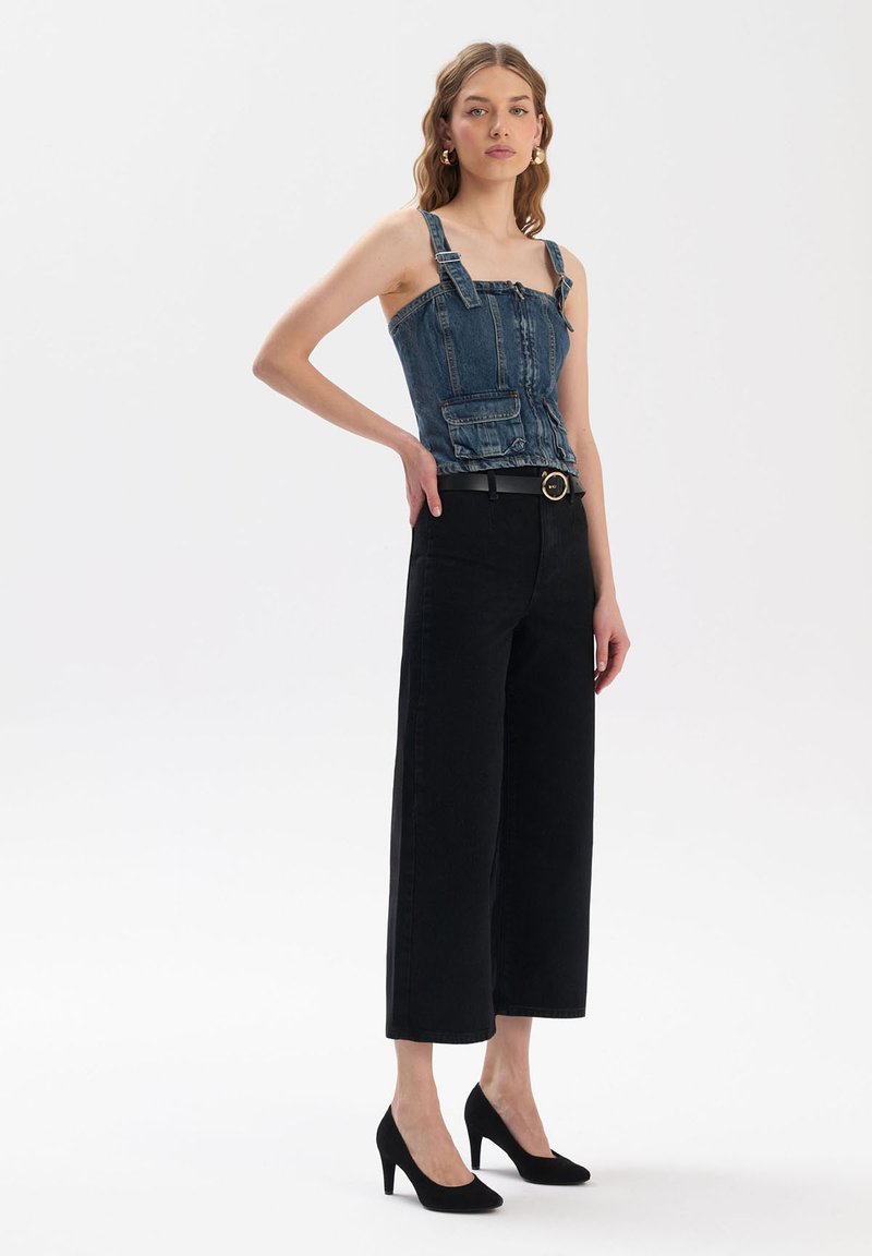 Denim korzetový top s ramínky a přední kapsou, zkombinovaný s černými kalhotami s vysokým pasem a širokými nohavicemi, doplněný černými lodičkami se špičatou špicí.