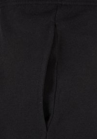 Close-up of a black fabric garment showing a vertical slit-style pocket with visible stitching along the edges.