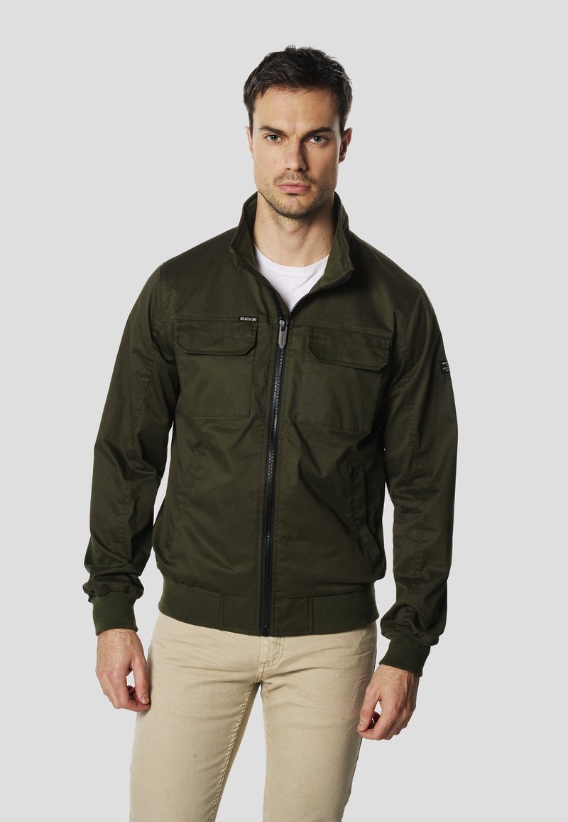 Kurtka typu bomber w kolorze oliwkowej zieleni z zamkiem błyskawicznym z przodu, dwoma kieszeniami na piersi, ściągaczami na mankietach i u dołu. Wykonana z gładkiej tkaniny o matowym wykończeniu.