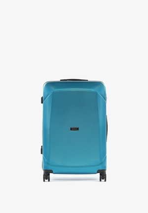 Niebieska walizka z twardą obudową o teksturowanej powierzchni, cztery czarne kółka obrotowe i centralna etykieta marki na przednim panelu.