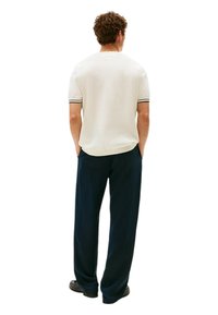 Camicia crema a maniche corte con rifiniture nere, abbinata a pantaloni ampi blu scuro. Il tessuto sembra morbido con una vestibilità comoda.