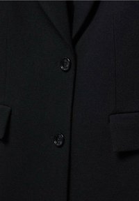 Zwarte blazer van een gestructureerde stof, met twee knopen en klepzakken. Strak ontwerp zonder zichtbare patronen of versieringen.