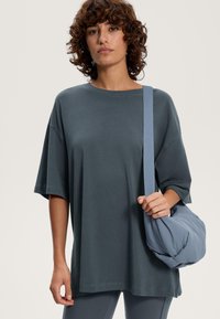 Överdimensionerad mörkgrå T-shirt med rund halsringning och korta ärmar, ihop med en ljusblå, vadderad axelremsväska i mjukt material.