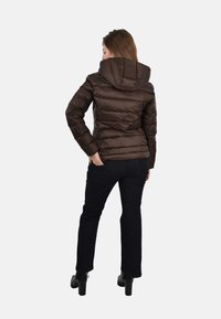 Hnedá bundá s kapucňou typu puff, so prešívanou textúrou a priliehavým strihom. V kombinácii s tmavými džinami a čiernymi lodičkami.