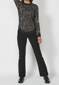 Pantalones acampanados negros combinados con un suéter difuso y multicolor que presenta un estampado de animales en forma de ondas y un dobladillo curvado.