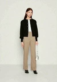 Melna, ar pogām priekšā, jaka pār baltu krekli; kopā ar bēšiem augstām, platiem biksēm un melnām kurpēm; tur rokā baltu somiņu.