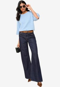 Pulover tricotat bleu deschis cu mâneci trei sferturi, combinat cu blugi dark denim cu picioare largi, curea maro și pantofi cu toc maro. Geantă neagră, ochelari de soare.