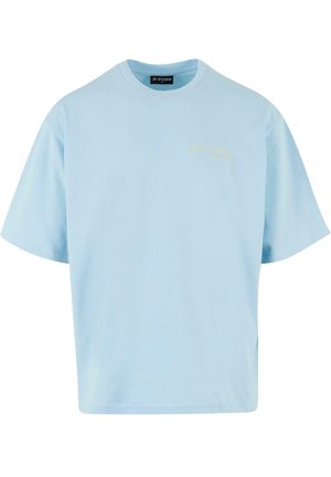 Világoskék, rövid ujjú pamut póló. Lazán illeszkedő fazonnal rendelkezik, és egy kis sárga logó található a bal felső mellkasi részen.