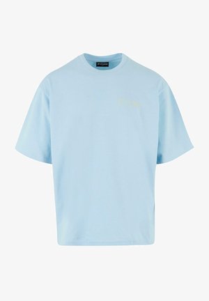 Világoskék, rövid ujjú pamut póló. Lazán illeszkedő fazonnal rendelkezik, és egy kis sárga logó található a bal felső mellkasi részen.