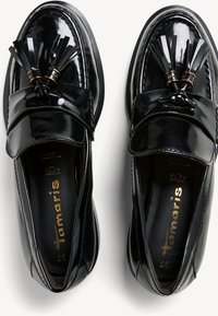 Sorte lakkpato sko med rund tå, dekorativ duskdetalj og sydd kantdetalj.
