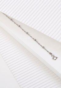 Pulsera de cadena de plata con acentos esféricos, que presenta una textura suave y un cierre de langosta. Ambientada sobre un fondo blanco y estriado.