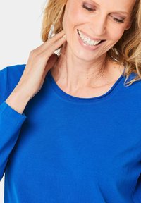 Blauw langmouwtop met een ronde hals en zachte katoen. Glad oppervlak met zichtbare stiksels langs de randen van de mouwen.