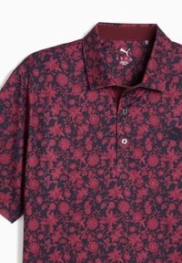 Marineblå polo skjorte med et all-over blomstermønster i nuancer af burgunder. Har en knapkrave og et logo-patch på venstre bryst.