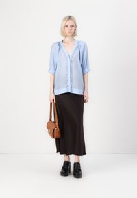 Lichtblauwe blouse met pofmouwen en kanten trim, gecombineerd met een bruine satijnen midi-rok en zwarte platform schoenen. Inclusief een bruine schoudertas.