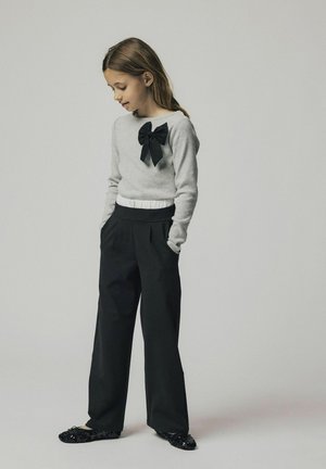 Maglione grigio con grande fiocco nero; cintura bianca; pantaloni neri a gamba larga; ballerine nere con paillettes. Palette di colori semplice e neutra.