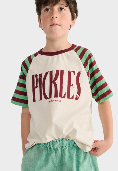 Ragazzo con capelli castani che indossa una maglietta crema con maniche a righe rosse e verdi e la scritta "PICKLES" in rosso sul davanti.