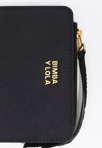Cartera de tela negra con letras doradas "BIMBA Y LOLA." Cuenta con un cierre de cremallera y una correa texturizada. Superficie suave y forma rectangular.