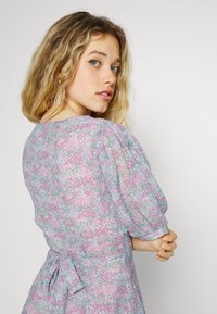 Vestuário floral com um padrão multicolorido de flores rosa, verdes e azuis, com mangas bufantes e um detalhe de cintura amarrada.