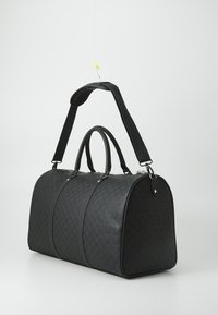 Borsa a duffle nera realizzata in materiale texturizzato, con una forma curvata, due manici superiori e una tracolla rimovibile. Dettagli di pattern sottili.
