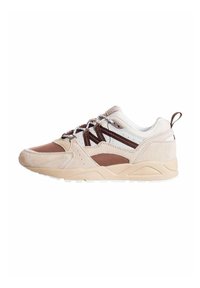 Scarpa da atletica beige e marrone con tomaia in rete, sovrapposizioni in suede e suola in gomma bianca testurizzata. Presenta lacci in contrasto e un linguetta posteriore.