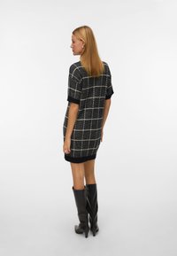 Melnā un baltā pārbaudītā raksta kleita ar īsām piedurknēm, ribotām aprocēm un apakšmalu. Apvienota ar melnām augstpapēžu zābakiem līdz ceļiem ar smailām pirkstiem. Gluda tekstūra.