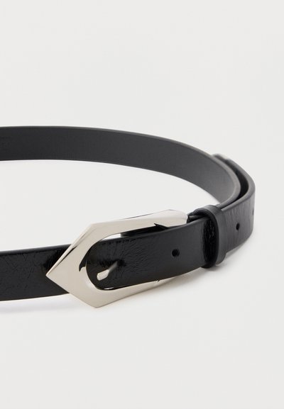 Μαύρη στενή δερμάτινη ζώνη με ασημένια γεωμετρική αγκράφα, μερικώς τυλιγμένη πάνω σε λευκό φόντο.