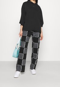 Svart Nike huvtröja, grå och svarta patchworkbyxor med fransade kanter, och vita sneakers. Bär en ljusblå axelväska.