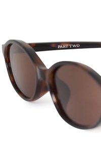 Lunettes de soleil rondes écaille avec verres marron foncé et « PART TWO » imprimé en blanc sur la branche.