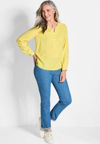 Blusa gialla a maniche lunghe con dettagli di bottoni, abbinata a jeans dritti blu e sneakers bianche. Tessuto morbido e vestibilità rilassata.