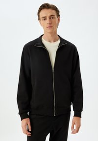 Svart zip-up sweatshirt med hög krage, ribbade manschetter och nederkant. Tillverkad av mjukt tyg med framfickor och en jämn textur.