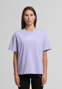 Šviesiai violetinė medvilninė T-Marškiniai su trumpomis rankovėmis, apvaliu kaklu ir baltu "Von Dutch" logotipu, kuris yra išdėstytas ant krūtinės. Tekstūruotas audinys, laisvas dėvėjimas.