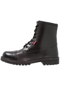 Bottes noires en cuir à la cheville avec un bout rond, une fermeture à lacets et une semelle en caoutchouc texturée. Présente une étiquette rouge sur le côté.