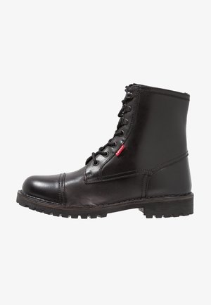 Bottes noires en cuir à la cheville avec un bout rond, une fermeture à lacets et une semelle en caoutchouc texturée. Présente une étiquette rouge sur le côté.