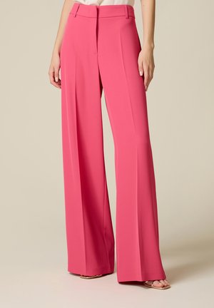 Roze broek met hoge taille en wijde pijpen, met plooien aan de voorkant, riemlussen en een verborgen sluiting aan de voorkant, gedragen met beige open teen hakken.