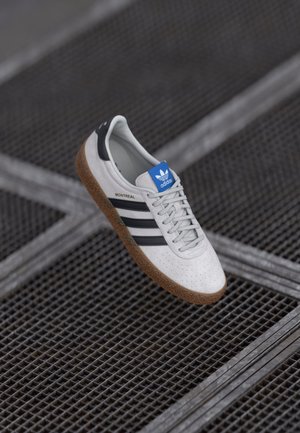 Hvide lædersneakers med sorte striber, grå snørebånd og et blåt logo. Har en struktureret gummisål og perforeret tåområde.