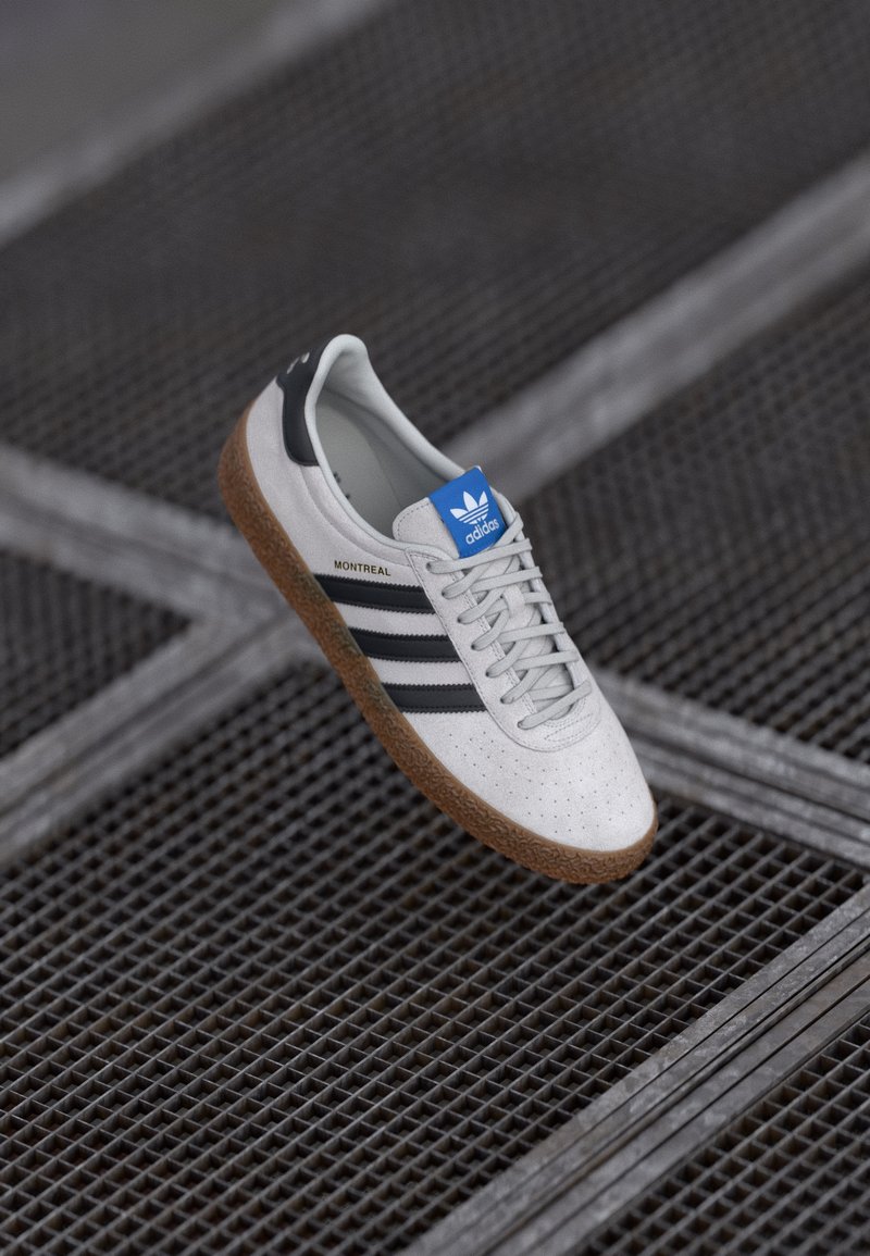 Hvide lædersneakers med sorte striber, grå snørebånd og et blåt logo. Har en struktureret gummisål og perforeret tåområde.