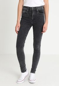 Jeans ajustados negros de mezclilla, con un diseño de cintura media, cinco bolsillos y un ligero desgaste, combinados con zapatillas blancas.