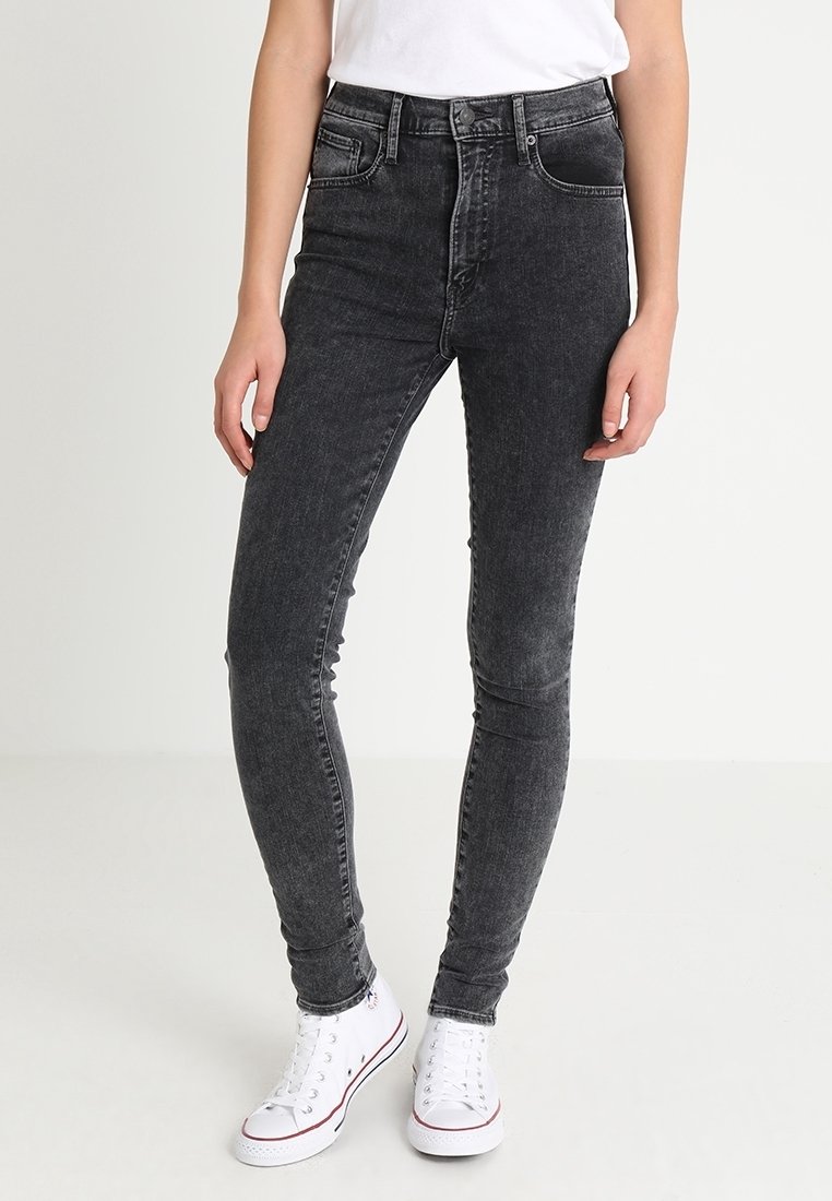 Jeans ajustados negros de mezclilla, con un diseño de cintura media, cinco bolsillos y un ligero desgaste, combinados con zapatillas blancas.