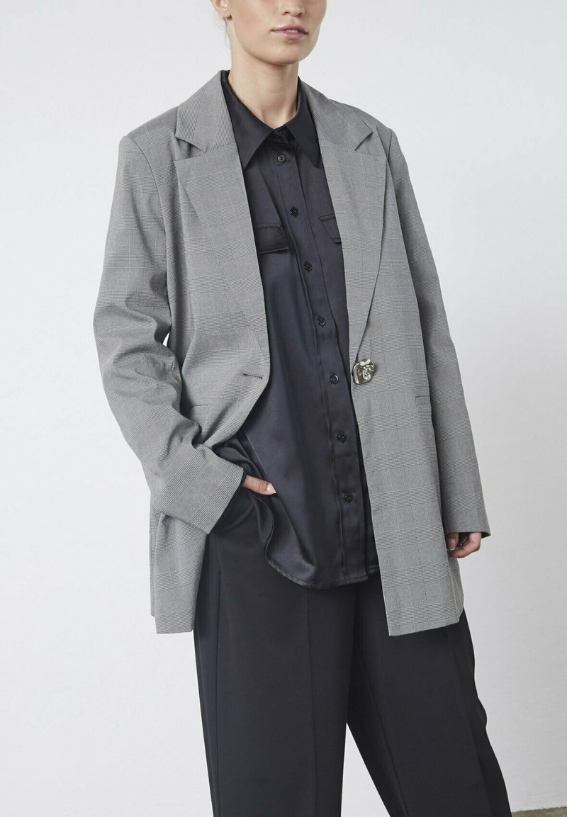 Gråternet blazer med en afslappet pasform, enkelt knaplukning og store klapkraver, parret med en sort satin skjorte med knaplukning.