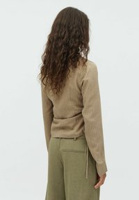 Top lungo beige a coste con vita aderente, abbinato a pantaloni verde oliva. Il tessuto presenta una sottile texture e un motivo.
