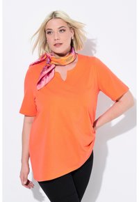 T-shirt a maniche corte e scollo a V in cotone arancione brillante con orlo curvo e vestibilità ampia, abbinato a una sciarpa rosa a fantasia.