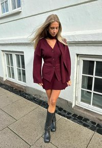 Burgundska pletena kardigan s velikim rukavima, uparen s odgovarajućom haljinom. Outfit upotpunjuju visoke crne čizme na visoku petu.