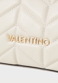 Gequilted crèmekleurige leren handtas met gouden "Valentino" logo in hoofdletters. Kenmerkt zich door een ruitpatroon en zichtbare stikdetails.